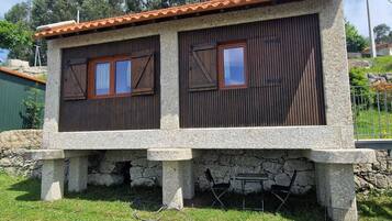 Un edificio de piedra con techo de tejas, dos ventanas de madera y base de piedra.