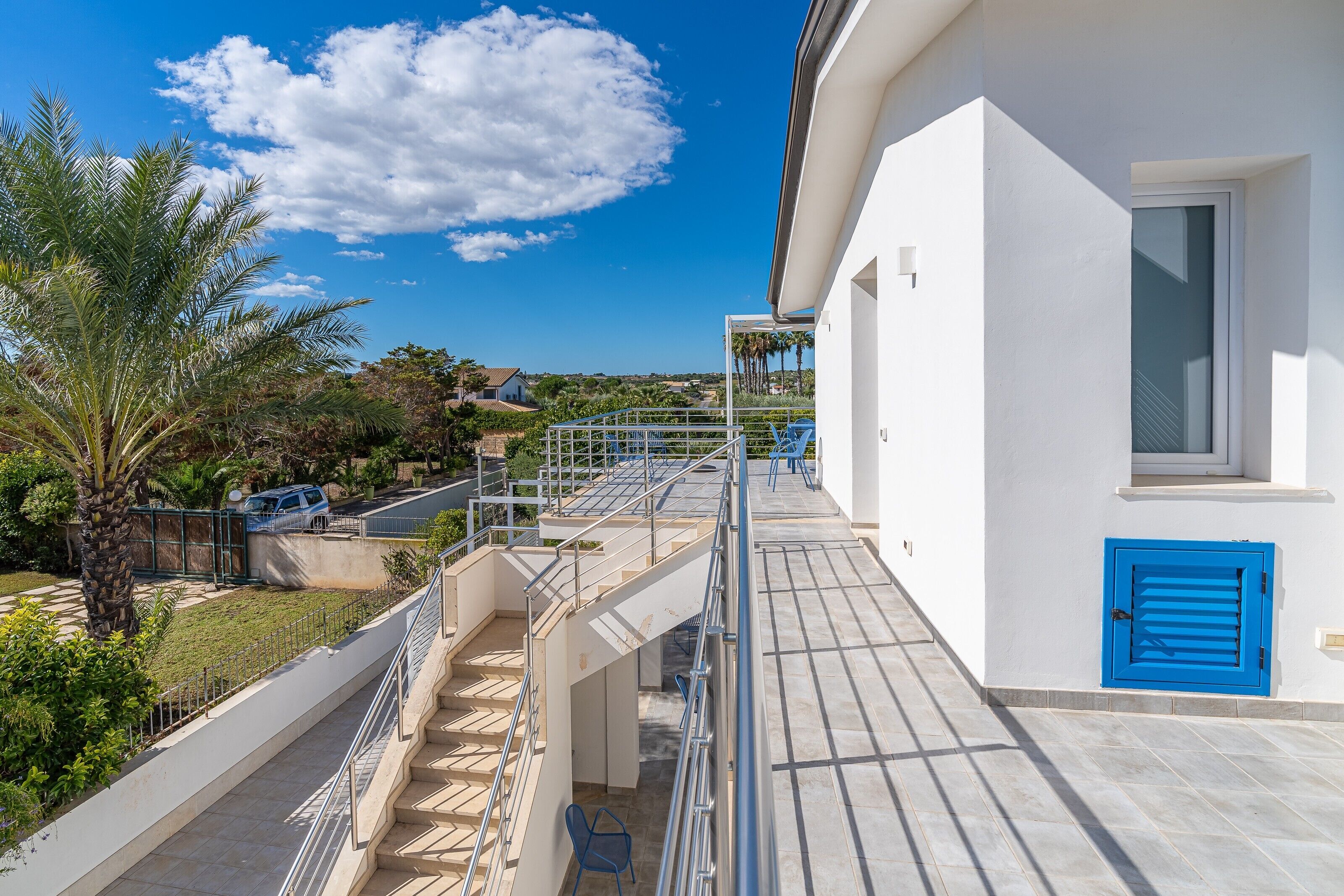 A modern building with a balcony, a blue door, and a staircase leading to an upper level.