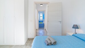 A bedroom with a bed, a nightstand, a lamp, a door leading to a bathroom, and a hallway.
