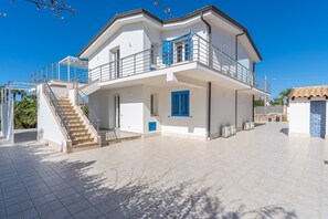 A two-story house with a balcony, a staircase, and a tiled patio.