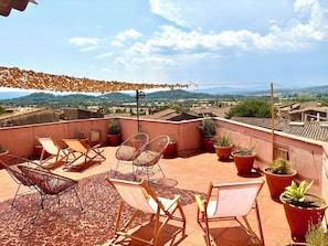 Eine Dachterrasse mit Außenmöbeln, Blumentöpfen und Blick auf die Landschaft.