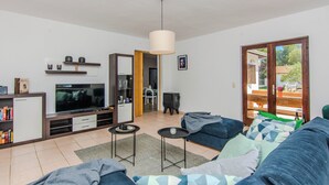 A modern living room with a sofa, TV, and a dining area visible through an open door. - Holiday home Kurta  (Privlaka)