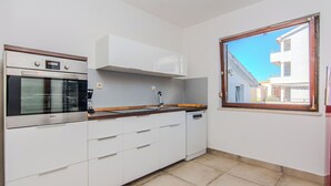 A kitchen with white cabinets, a built-in oven, and a window with a view of buildings. - Holiday home Kurta  (Privlaka)
