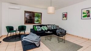 A living room with a black sofa, two green armchairs, a coffee table, a side table, and a large window with a view of trees. - Holiday home Kurta  (Privlaka)