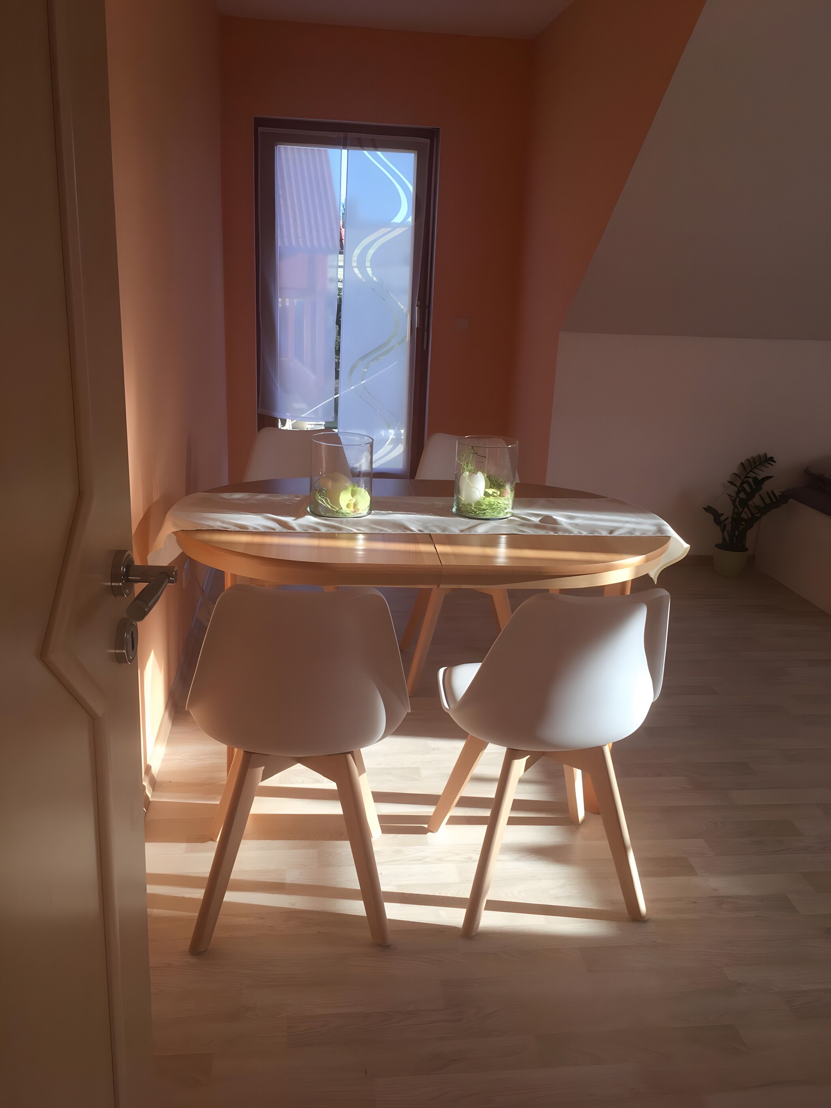 Un coin repas avec une table ronde, deux chaises et deux vases en verre contenant des fleurs.