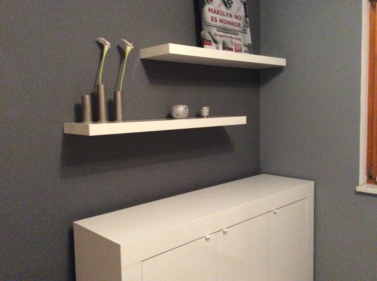 Um armário branco com gavetas, duas prateleiras brancas com objetos decorativos, e uma parede cinzenta.