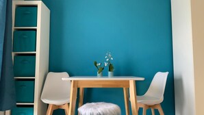 Ein Zimmer mit einer türkisblauen Wand, weißen Stühlen, einem Holztisch und einem weißen Schrank mit türkis-farbenen Aufbewahrungsboxen.