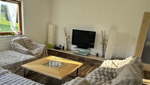 Ein gemütliches Wohnzimmer mit einem Flachbildfernseher, einem Holztisch und zwei bequemen Sesseln.