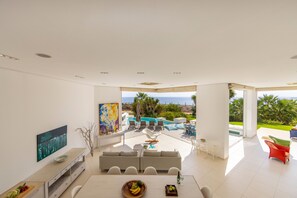 A modern living room with a large window, a pool, and outdoor seating. - Protaras Seafront Villa Alemar (Paralimni)