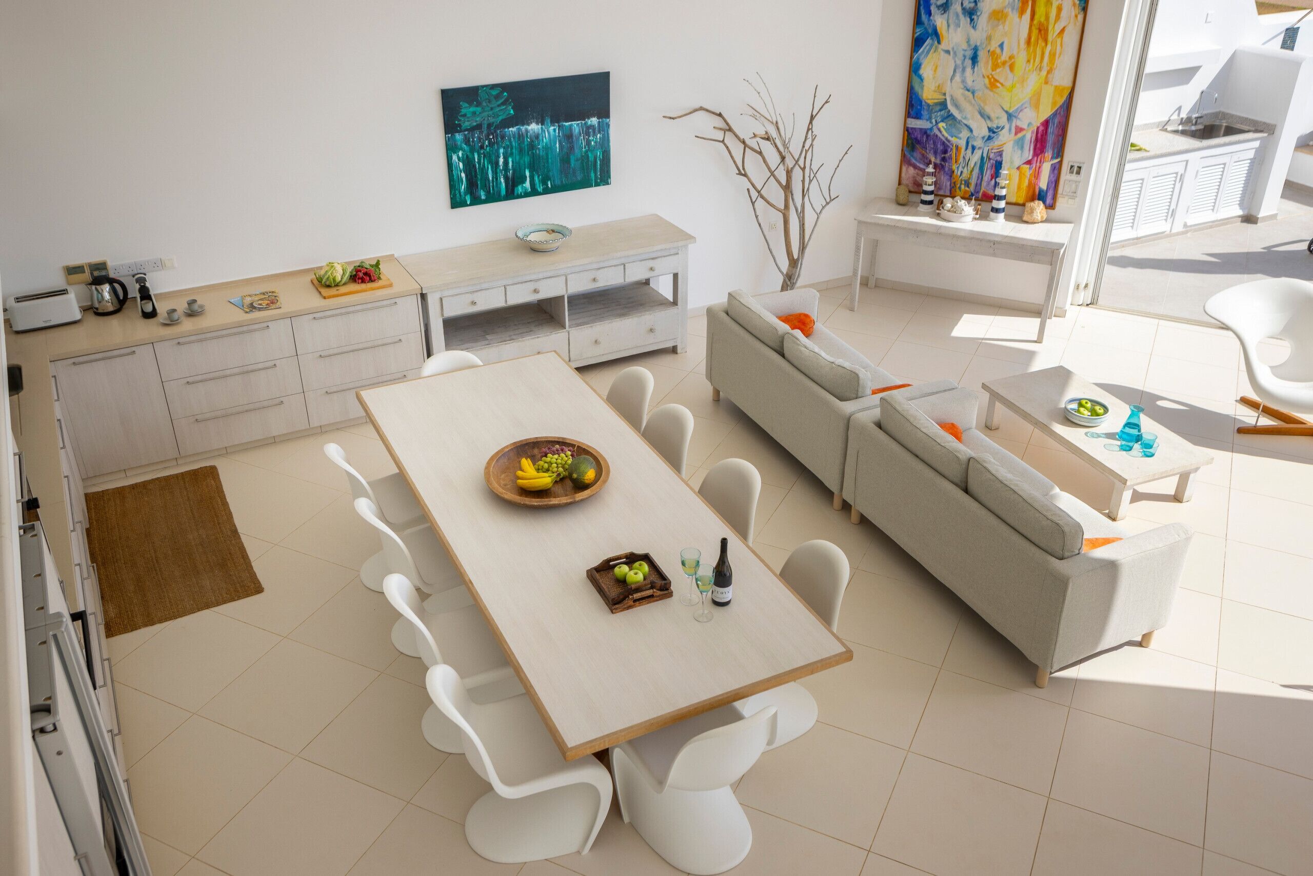 A modern kitchen with white cabinetry, a dining table with chairs, a sofa, and a large window.