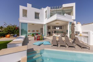 A modern house with a swimming pool, outdoor seating, and a spacious kitchen area. - Protaras Seafront Villa Alemar (Paralimni)