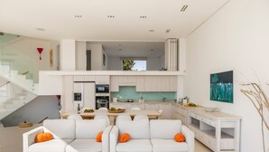 A modern, open-plan living area with a dining table and two white sofas with orange cushions. - Protaras Seafront Villa Alemar (Paralimni)