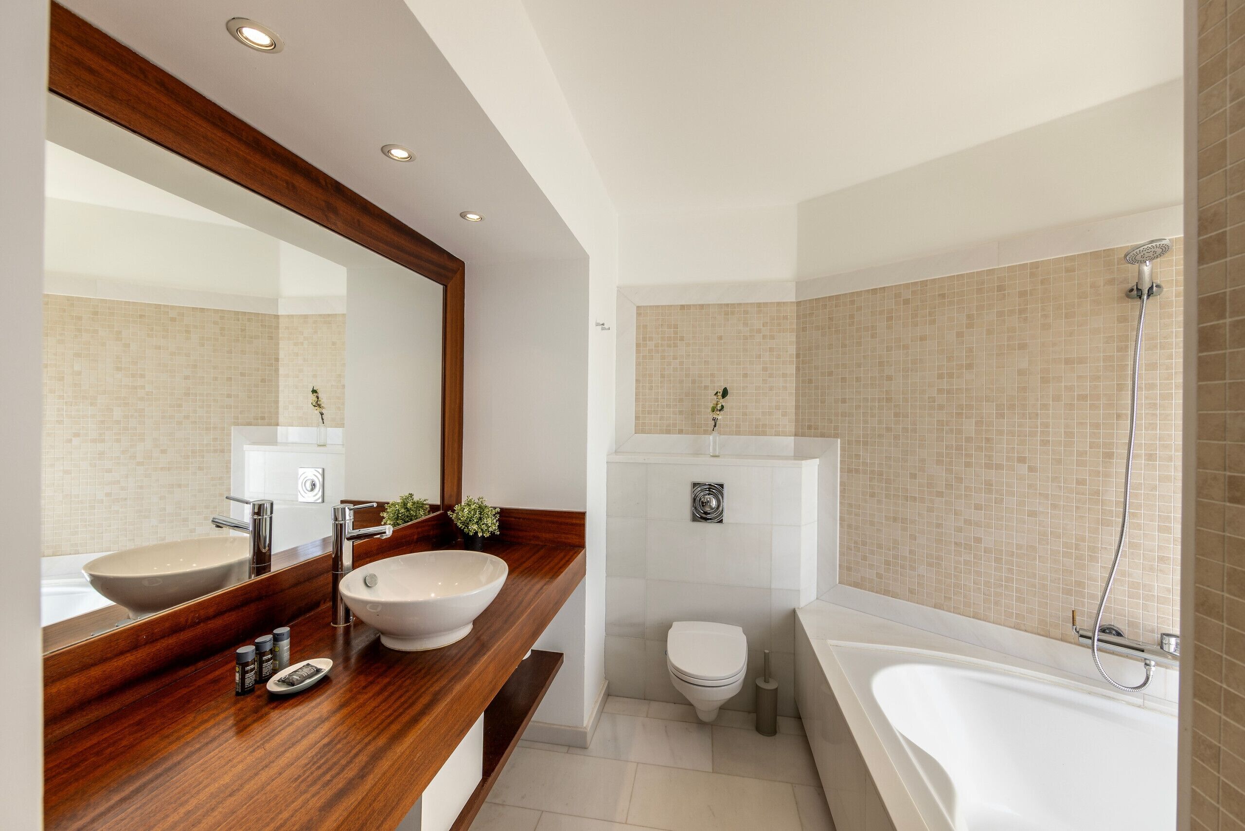 A modern bathroom with a wooden vanity, two sinks, a toilet, and a bathtub.