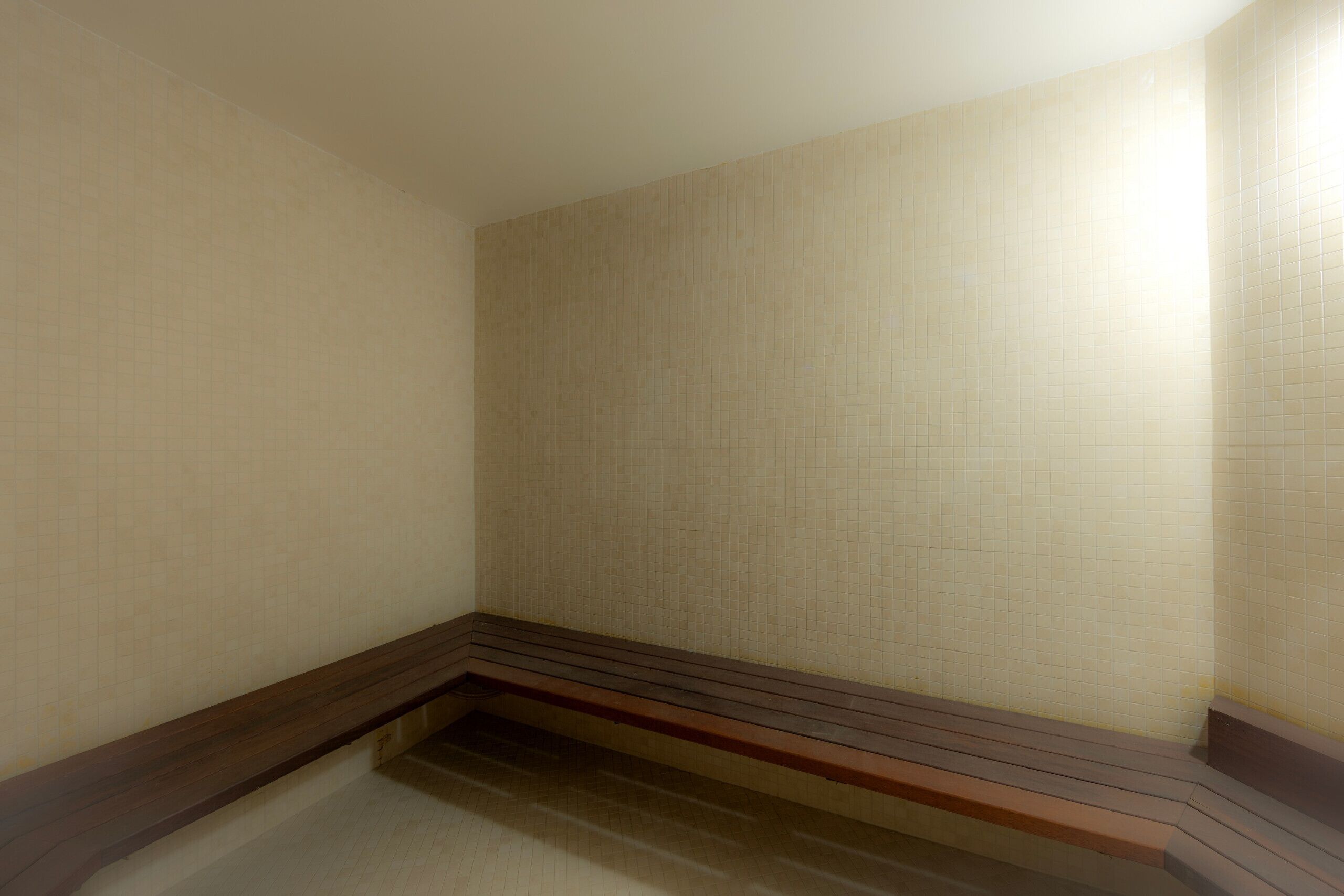 Rincón de una habitación con paredes de baldosas color beige y un banco de madera.