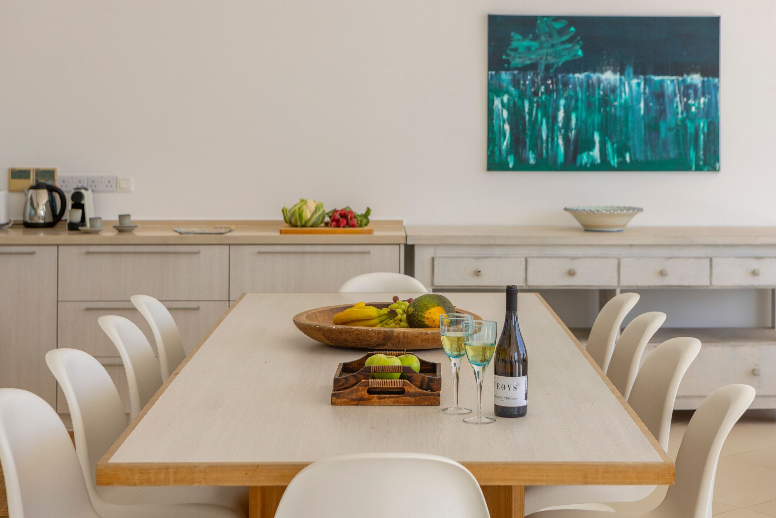 A dining table with a bottle of wine, glasses, and a fruit bowl.