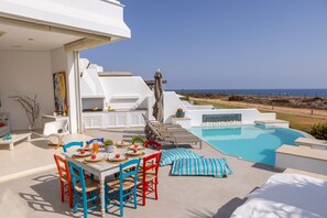 A modern outdoor dining area with a pool, white architecture, and a view of the sea. - Protaras Seafront Villa Alemar (Paralimni)