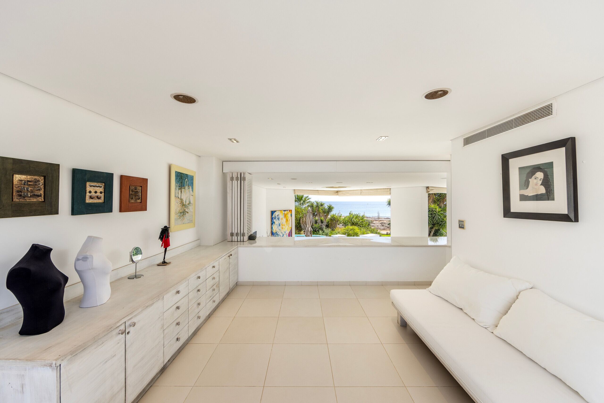 A modern living room with a white sofa, a dining area with a marble countertop, and artwork on the walls.