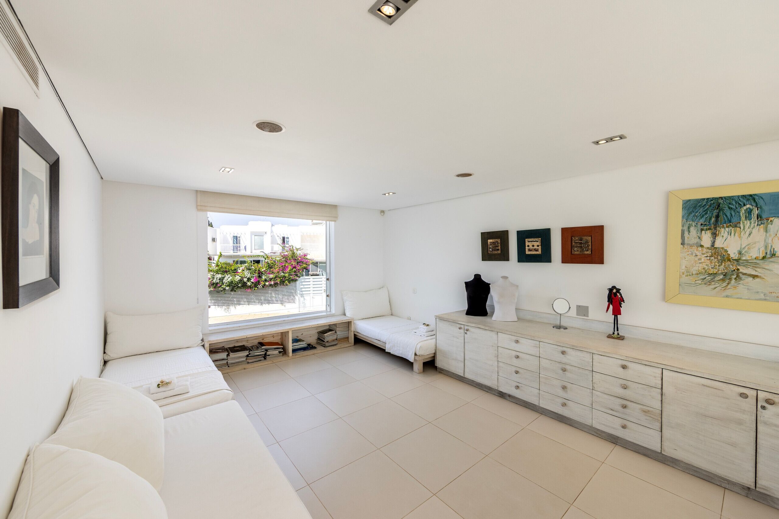 A modern living room with a sofa, a small bed, a cabinet, and a window with a view of a balcony.