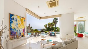A modern living room with a large painting, a pool, and a view of the ocean. - Protaras Seafront Villa Alemar (Paralimni)