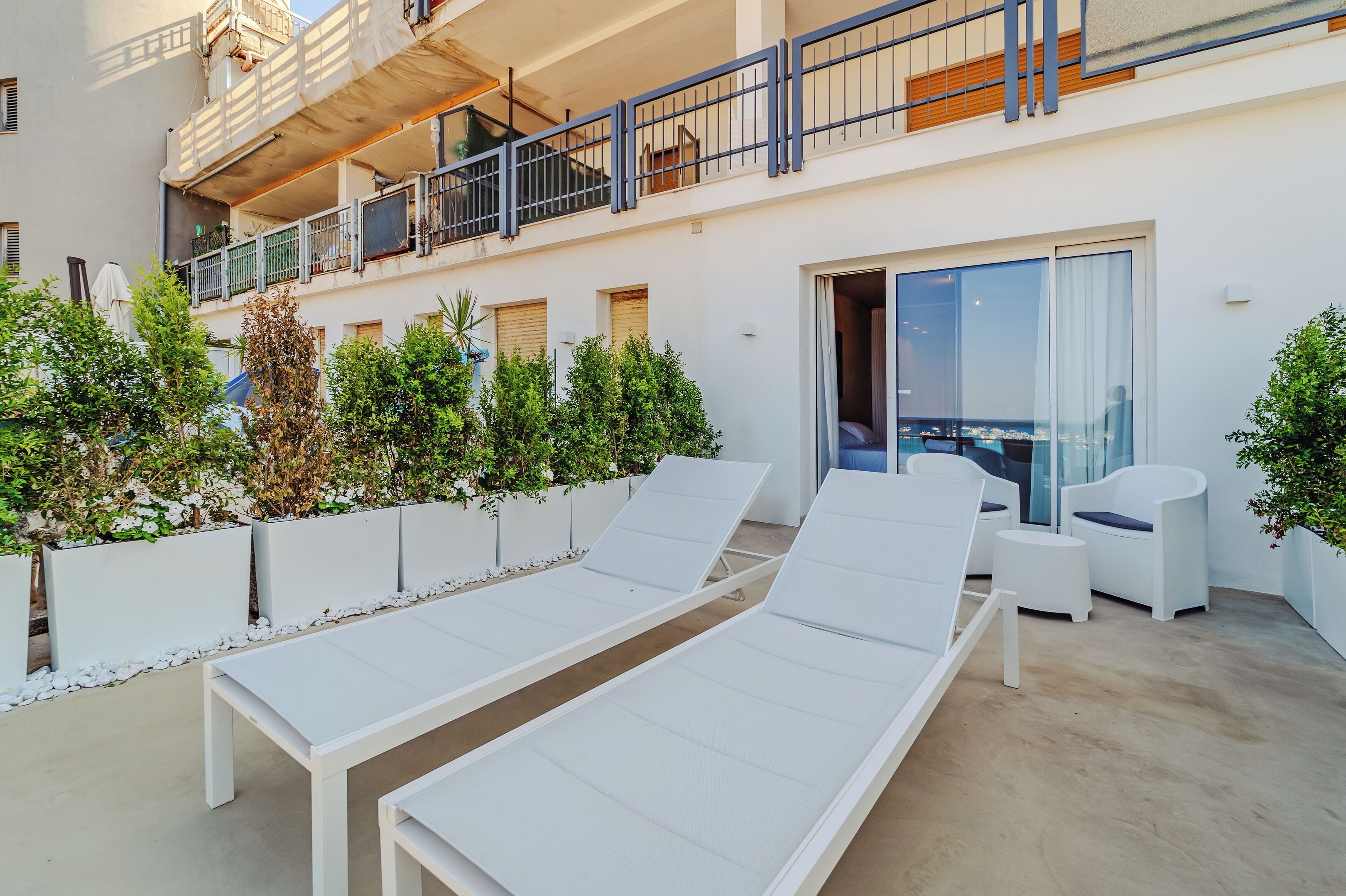 Een modern buitenzitgedeelte met witte loungestoelen en een kleine zithoek, omringd door plantenbakken en uitzicht op de stad.