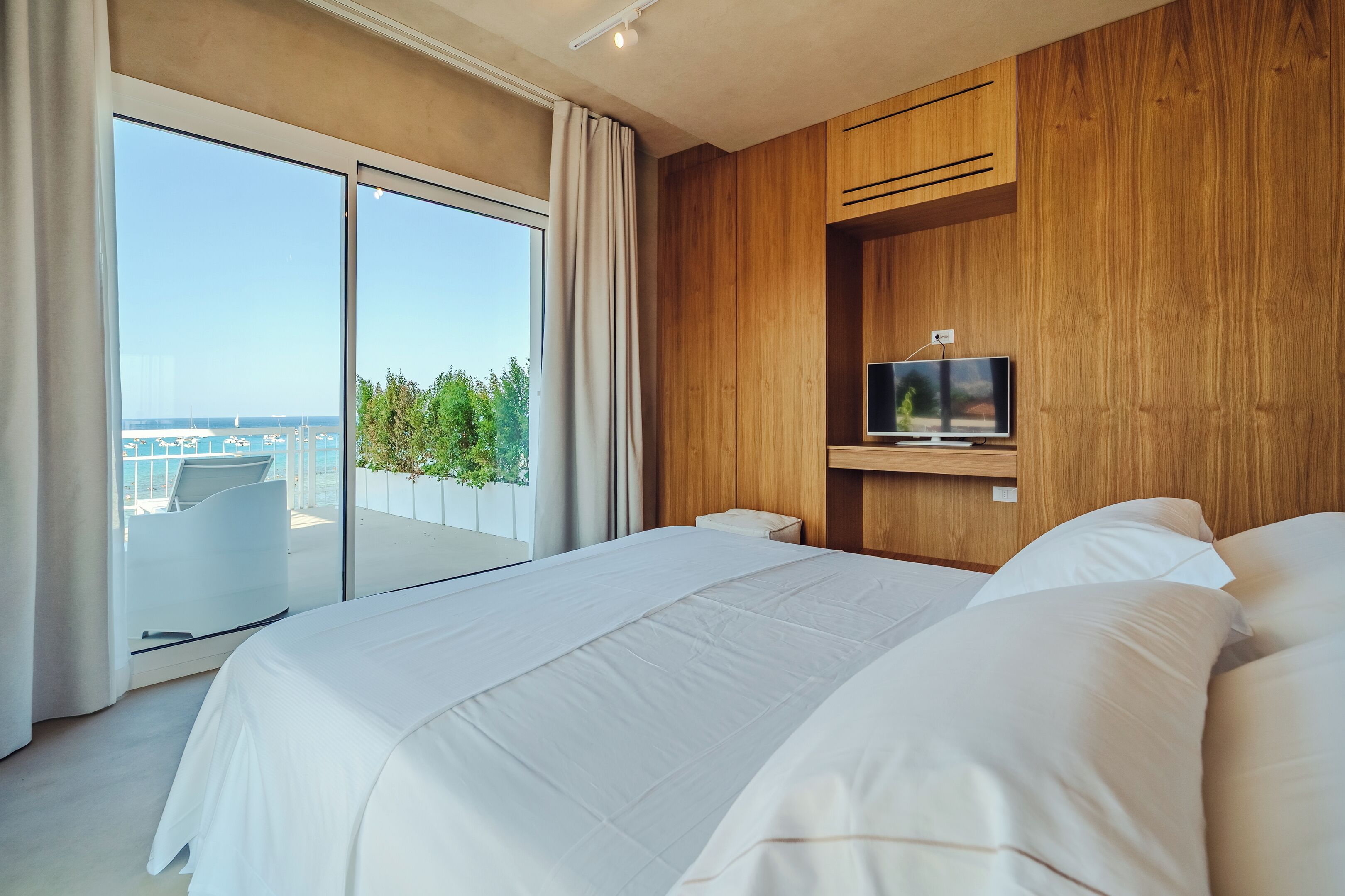 Una moderna camera d'hotel con un letto grande, una TV fissata a un pannello di legno e un balcone con vista sulla città.