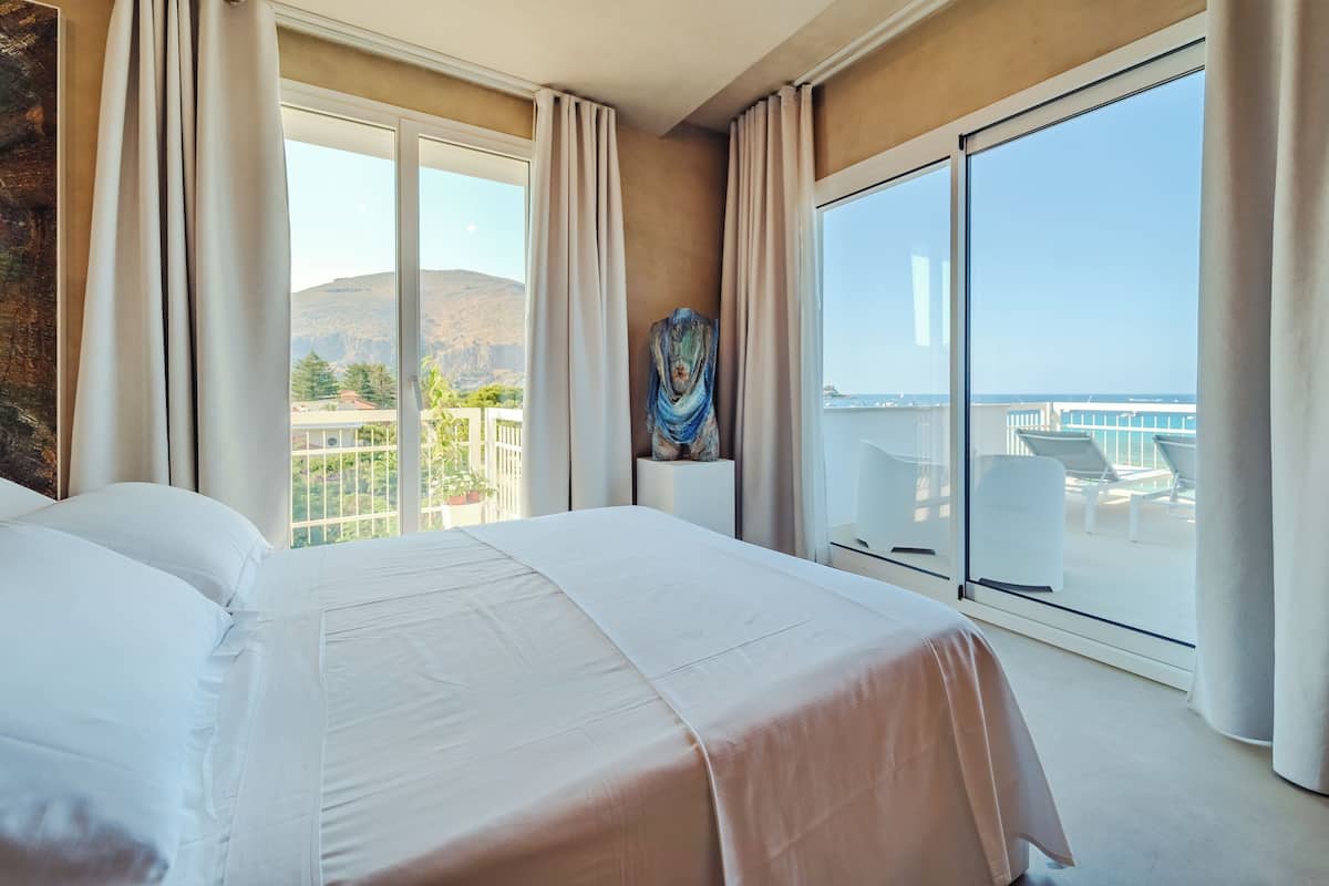 Een hotelkamer met een groot bed, uitzicht op zee en een balkon met buitenmeubilair.
