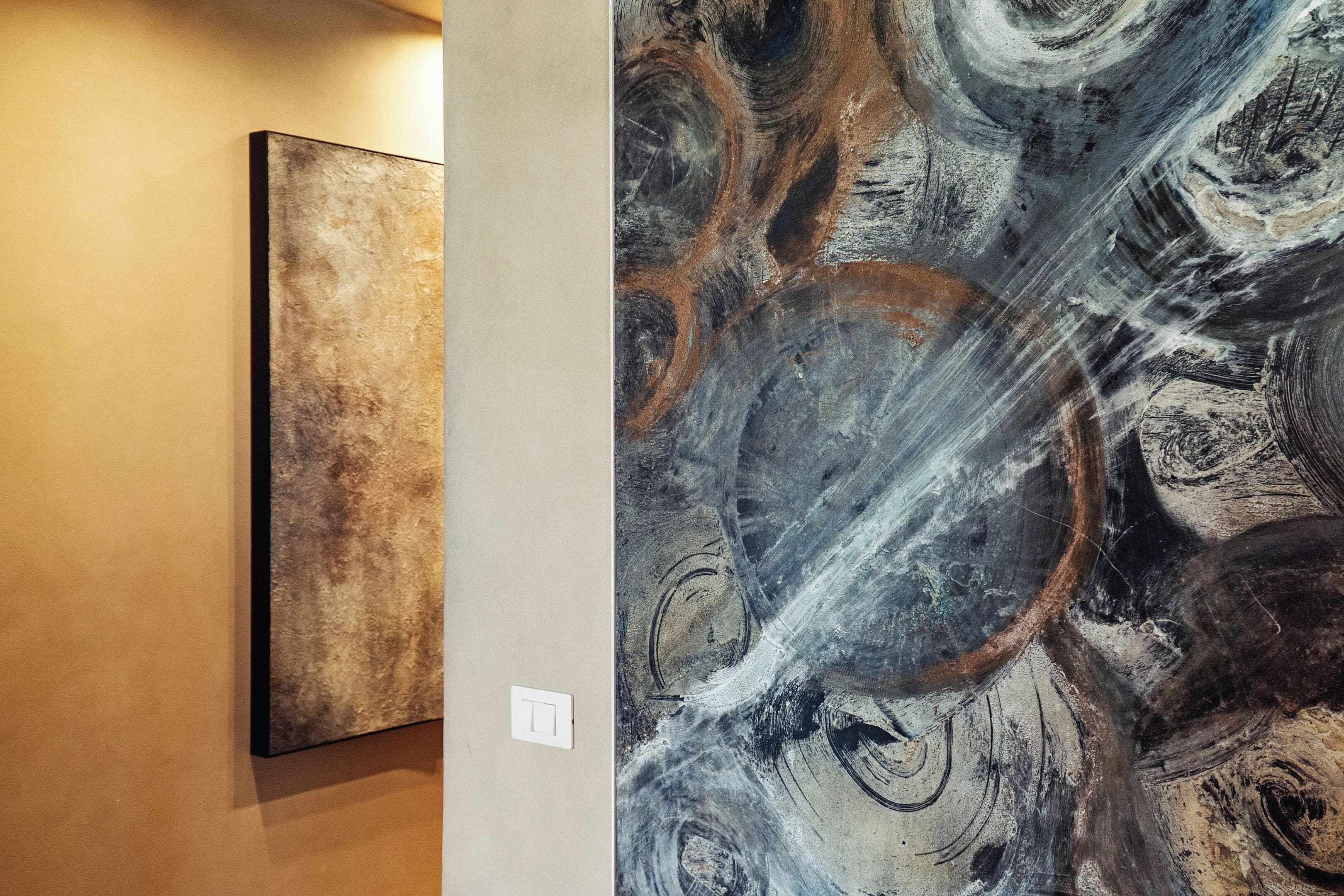 A wall with two artworks, one abstract and one with swirling patterns.
