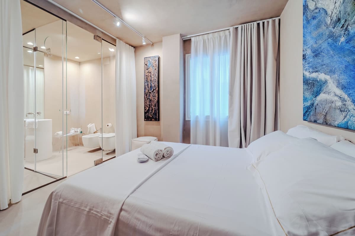 Een moderne hotelkamer met een groot bed, een douchecabine van glas, een schilderij aan de muur en uitzicht op de omgeving.