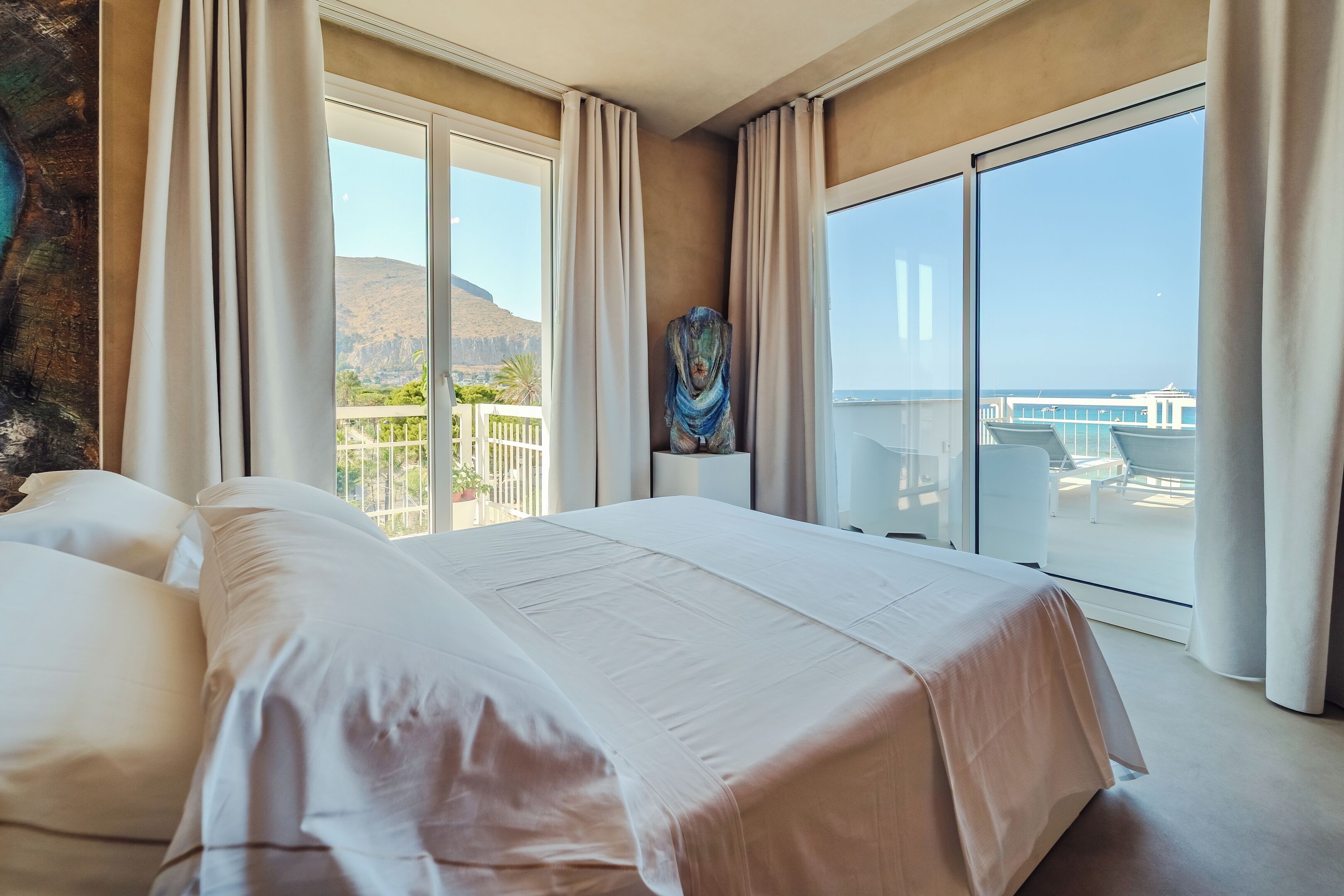 A hotel room with a large bed, a view of the sea, and a balcony with outdoor furniture.