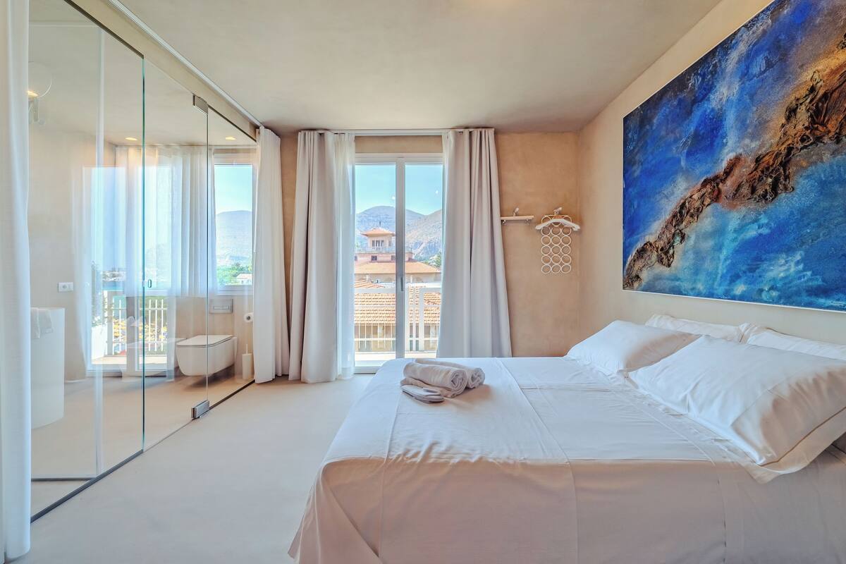 Een moderne hotelkamer met een groot bed, een glazen deur naar een balkon en een schilderij aan de muur.