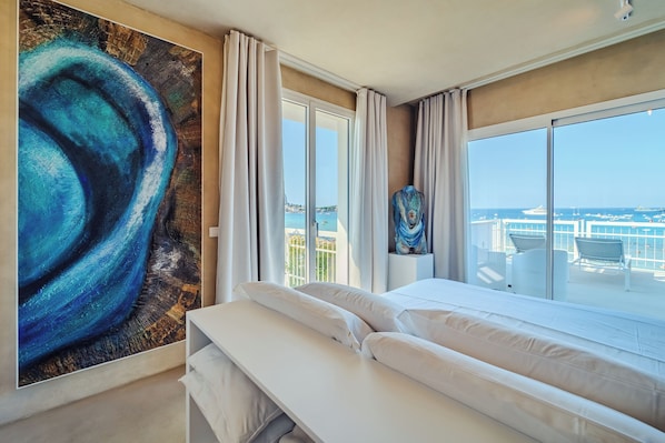 Habitación de hotel con una ventana grande, una cama, un cuadro y vista al mar.