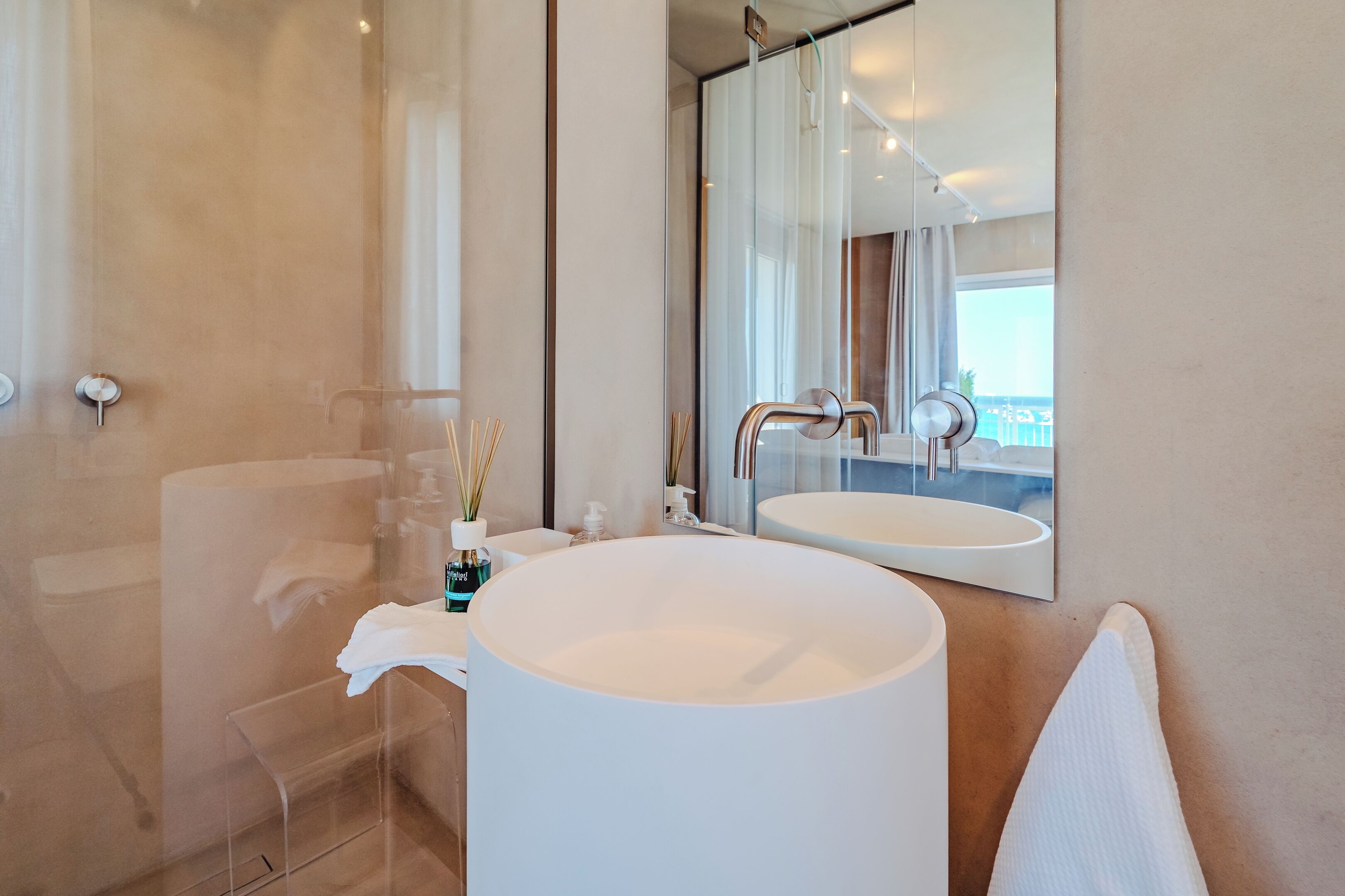 A modern bathroom with a large mirror, a round sink, and a glass shower enclosure.