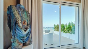 A modern room with a large glass door leading to a balcony with a view of the sea and greenery. - Hybrid Icon Rooms Gallery (Palermo)