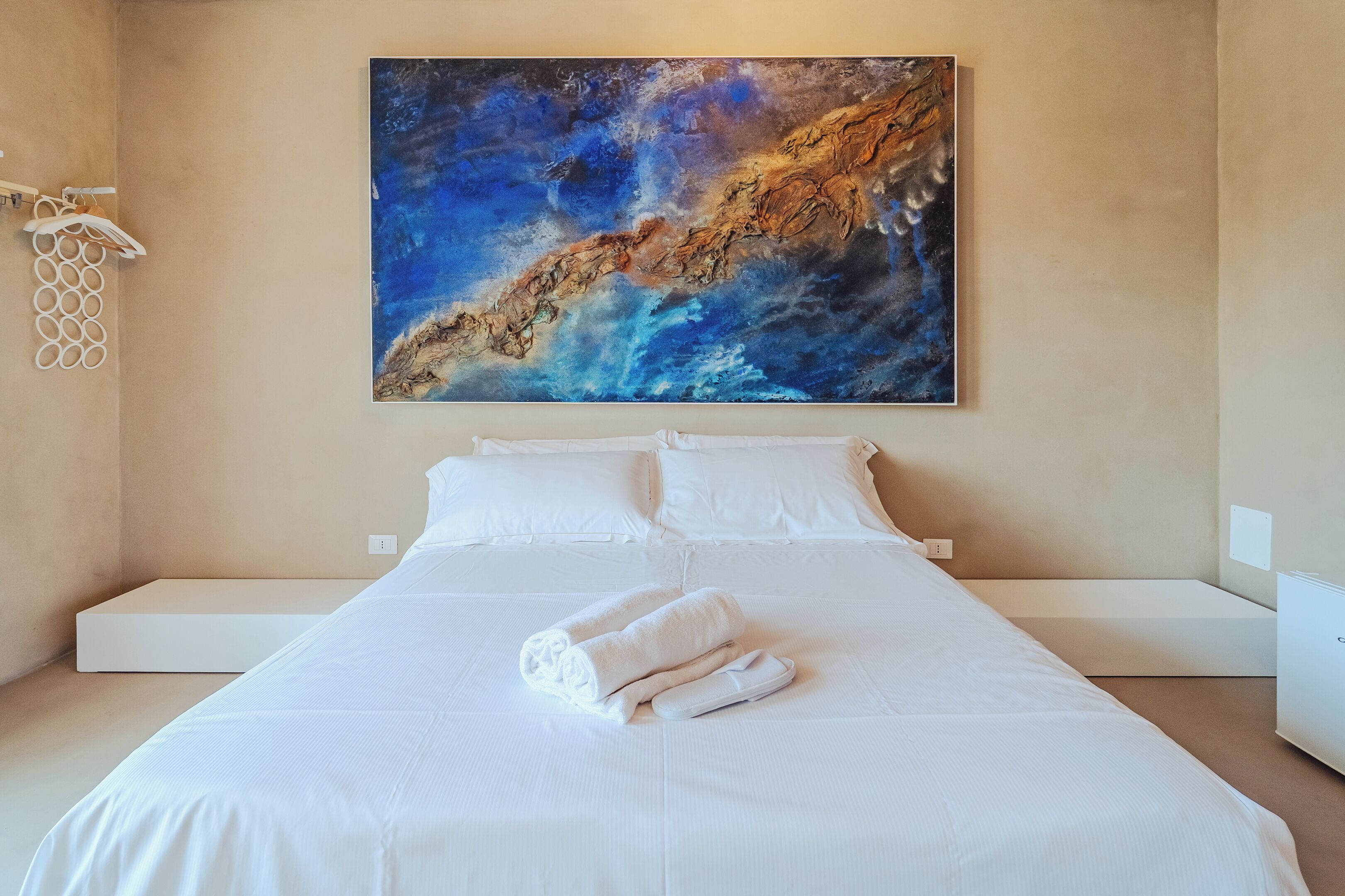 Ein Hotelzimmer mit einem großen Bett, weißen Leinentüchern, einem ordentlich gefalteten Handtuch und einem Gemälde über dem Bett.
