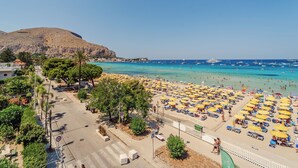 A beach with numerous sunbeds and umbrellas, a clear blue sea, and a mountain in the background. - Hybrid Icon Rooms Gallery (Palermo)