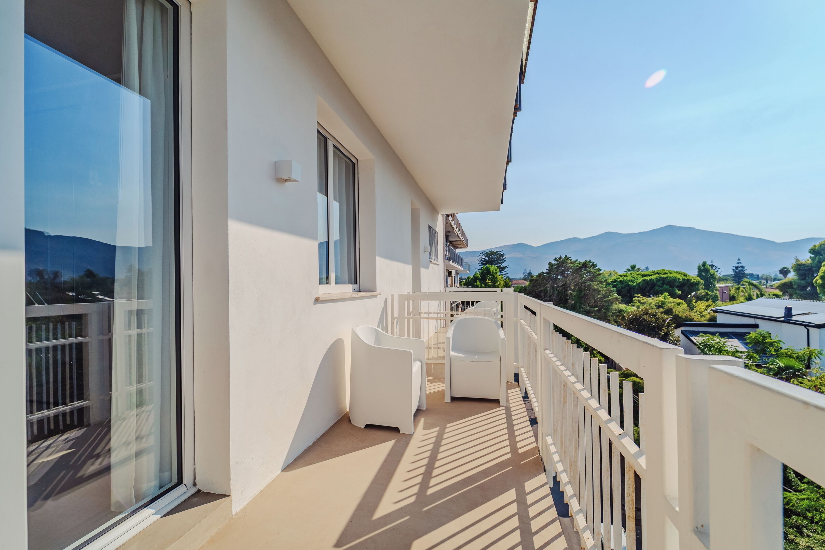 A balcony with white railings, two white chairs, and a view of mountains and greenery.