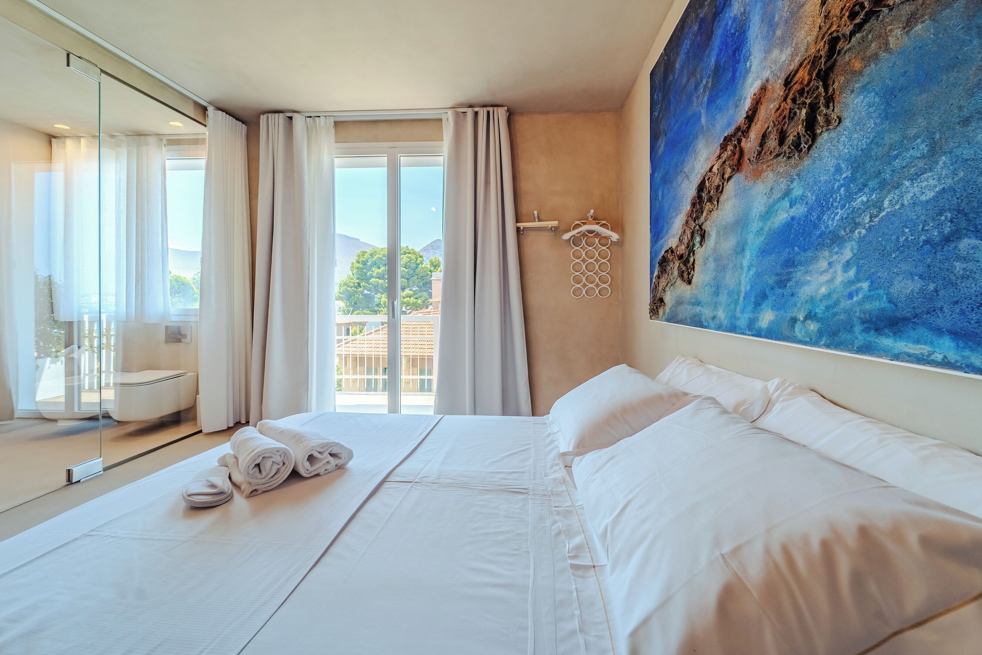 Une chambre d’hôtel avec un grand lit, une douche en verre et un tableau représentant un paysage bleu accroché au mur.