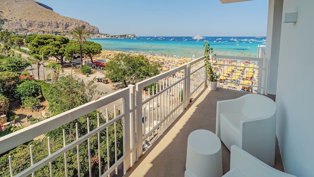 A balcony with white chairs, a view of a beach with umbrellas, and boats on the water. - Hybrid Icon Rooms Gallery (Palermo)