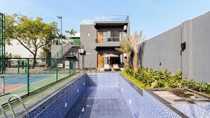 Ein modernes Gebäude mit Poolanlage, darunter ein blau fliesiger Pool, ein grüner Zaun und eine Treppe, die zu den oberen Etagen führt.