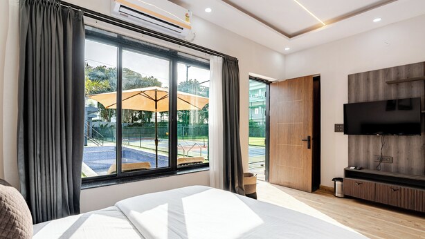 A modern hotel room with a large bed, a TV, and a view of an outdoor area with umbrellas.