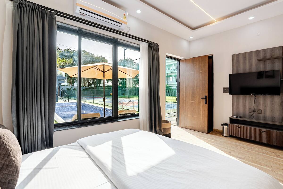 A modern hotel room with a large bed, a TV, and a view of an outdoor area with umbrellas.