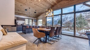 Eine moderne Küche mit einer zentralen Kochinsel, einem Essbereich mit Holztisch und -stühlen sowie großen Fenstern mit Blick auf die Berge.