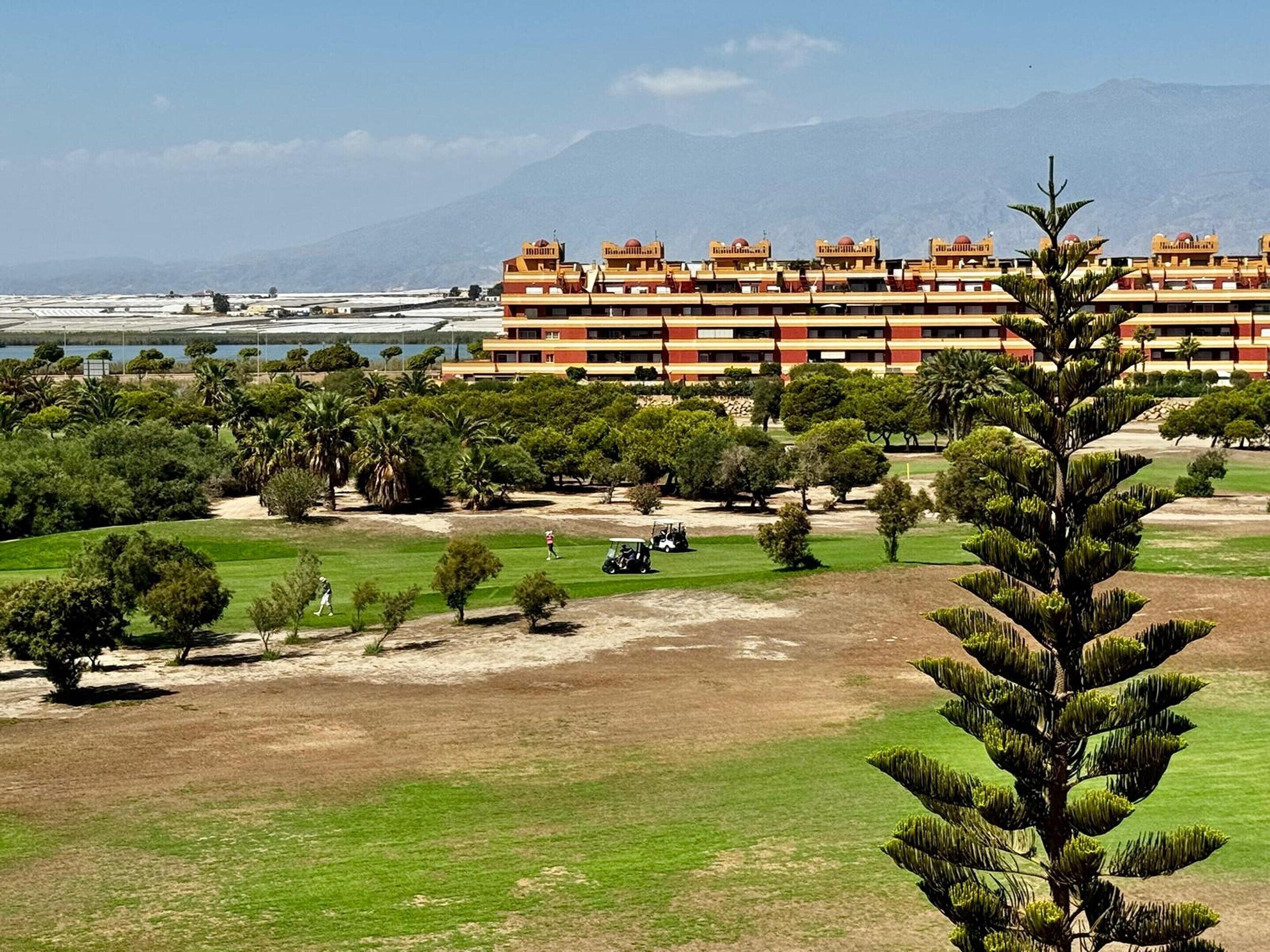 Een hotel met meerdere verdiepingen, een golfbaan en een bergachtig achtergrond.