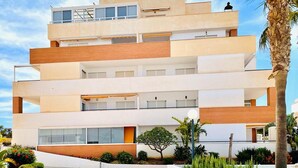 A multi-story building with balconies, large windows, and a landscaped garden. - Nice Apartment With Shared Pool (Roquetas de Mar)