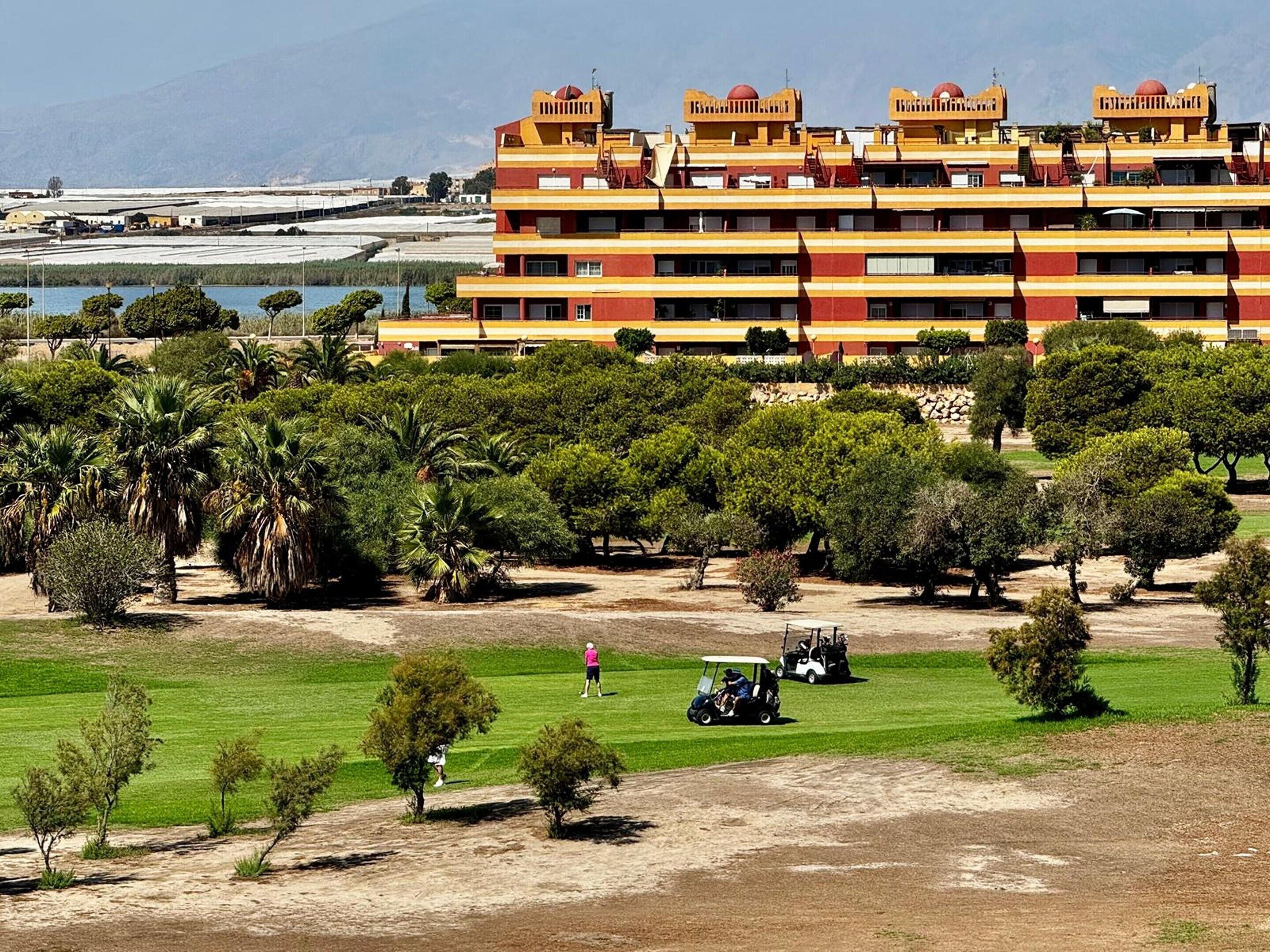 A multi-story hotel with a flat roof and a pool in the background.
