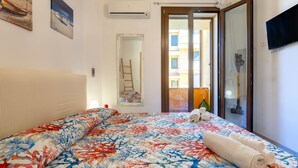 Une chambre d’hôtel équipée d’un lit, d’une télévision, d’une fenêtre donnant sur des immeubles et d’un appareil de climatisation.