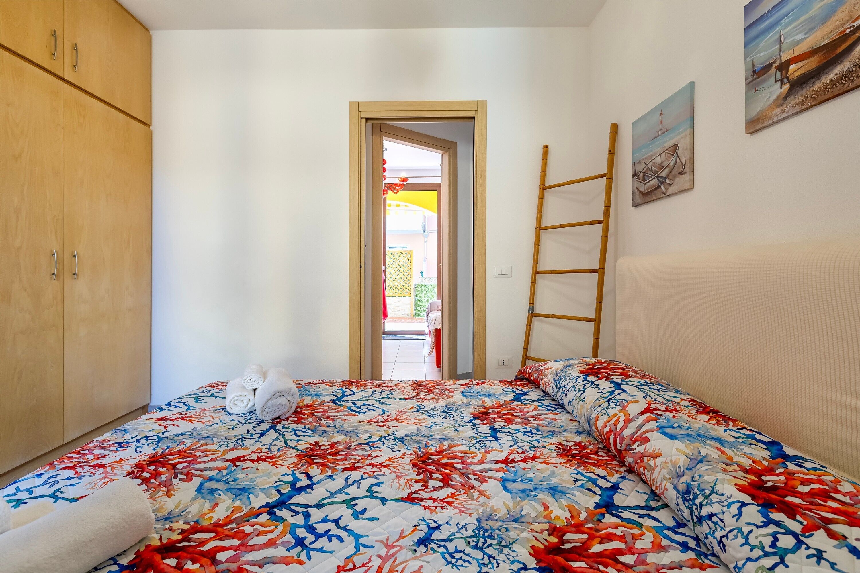 A bedroom with a bed, a wardrobe, a door leading outside, and a painting on the wall.