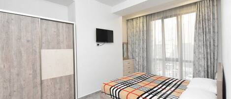 A bedroom with a bed, a wardrobe, a television, and a window with curtains.