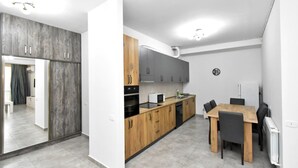 A modern kitchen with wooden cabinets, a built-in oven, and a dining area with a table and chairs. - Apartment by Luxe Group DI412 (Yerevan)
