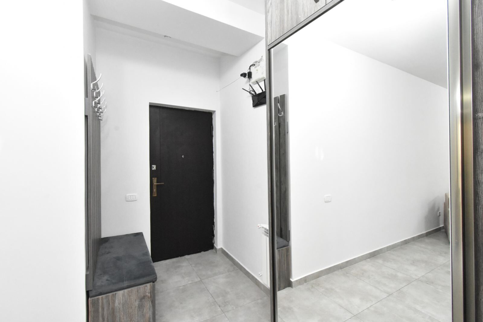 Un couloir moderne avec une porte noire, une petite poubelle et un miroir accroché au mur.